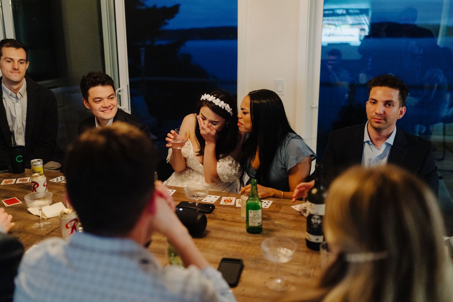 An evening wedding reception with guests gathered around a wooden dining table.