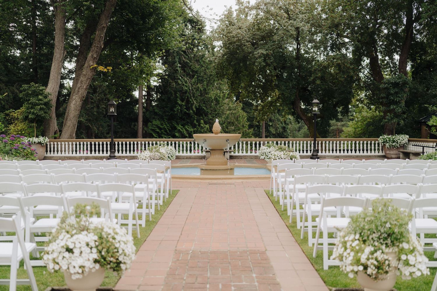 White chairs arranged outdoors for a garden wedding ceremony with floral decorations.