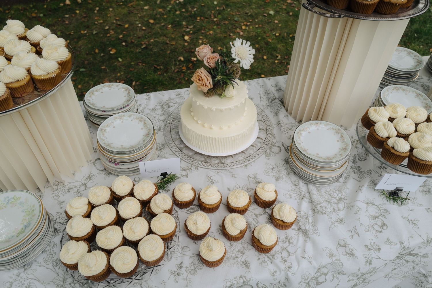 Wedding dessert table with white cake and cupcakes displayed on lace tablecloth.