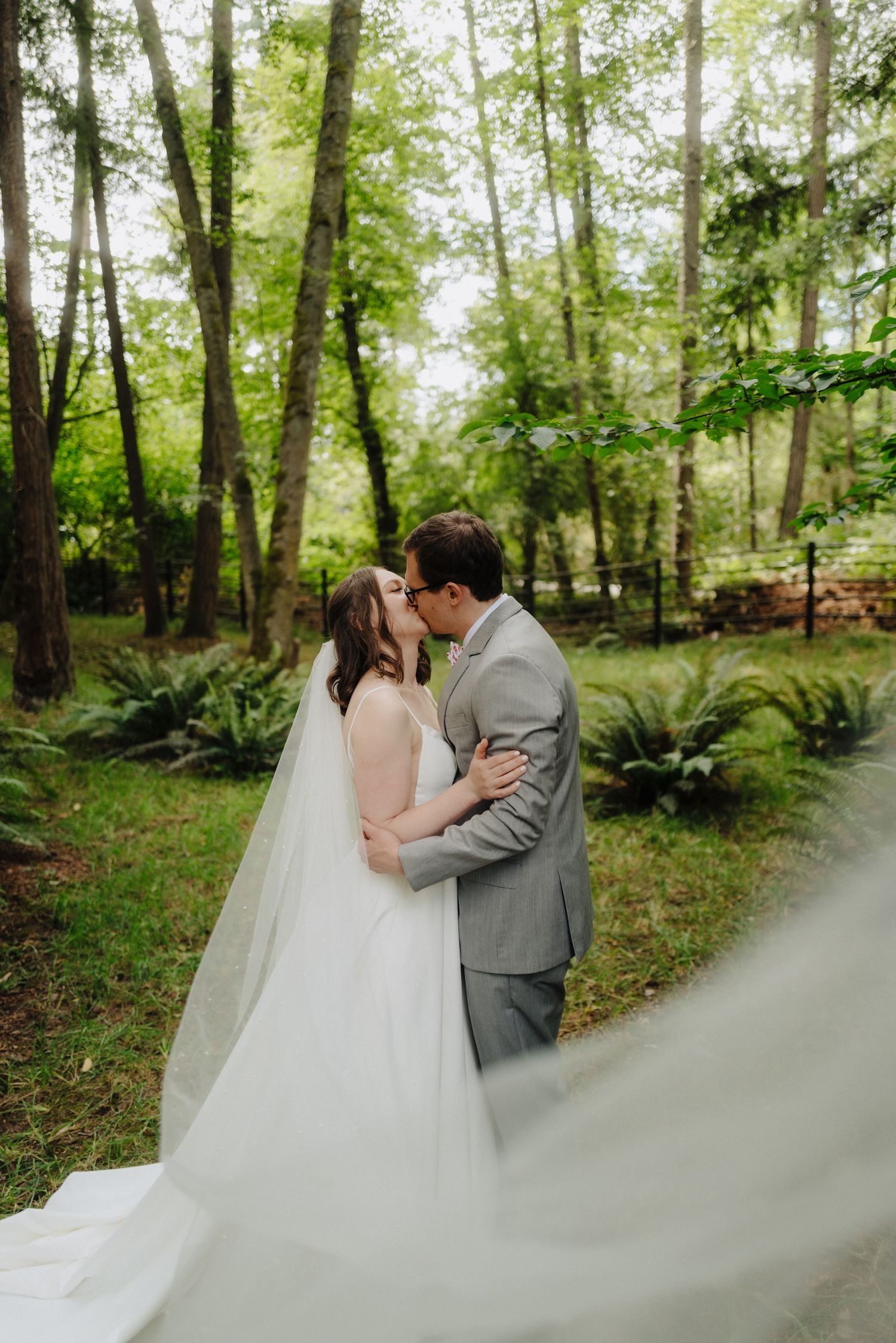 A flowing white wedding dress train creates an ethereal effect in a wooded forest setting.