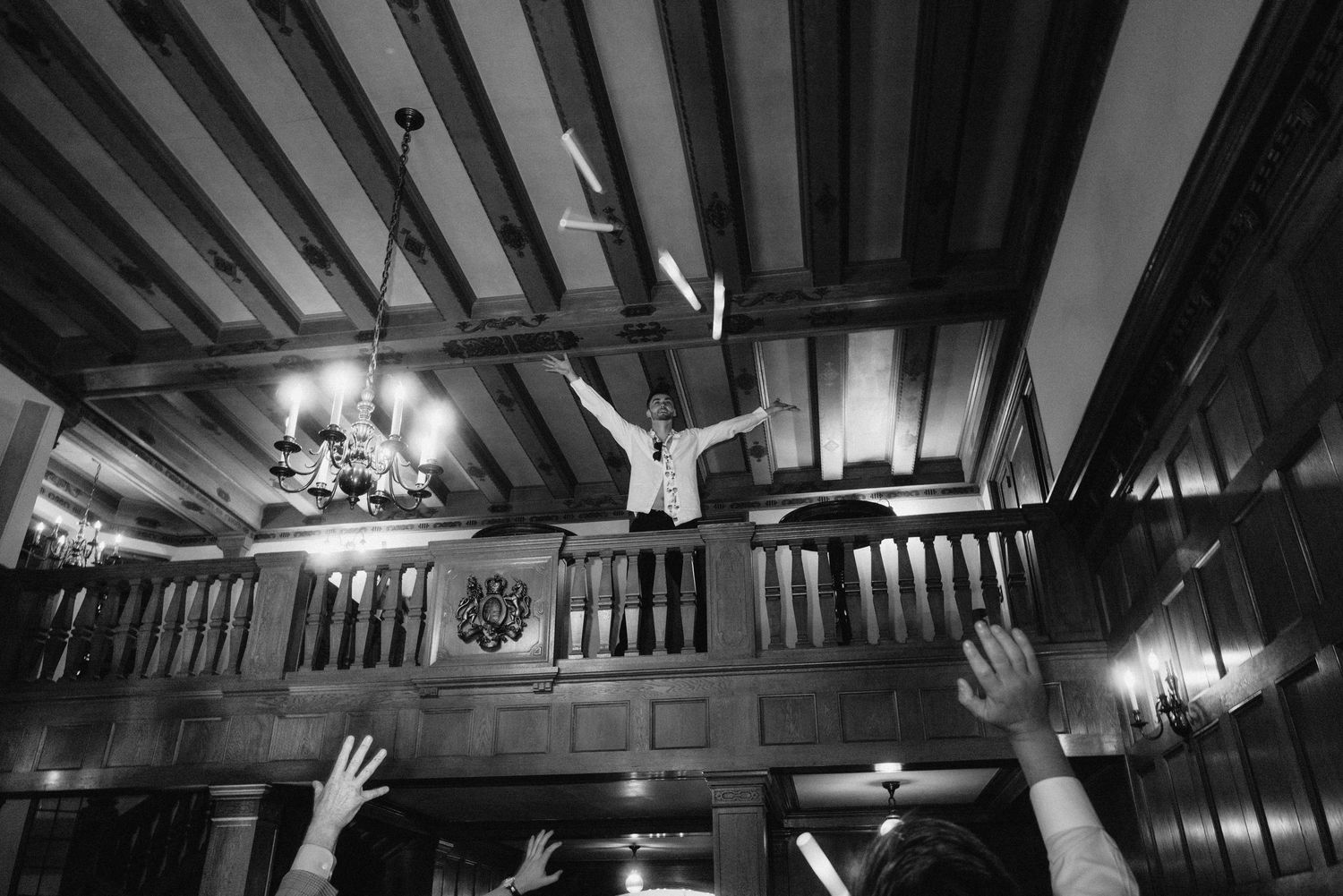 Black and white photo of wedding reception venue with exposed wooden beams and chandeliers.
