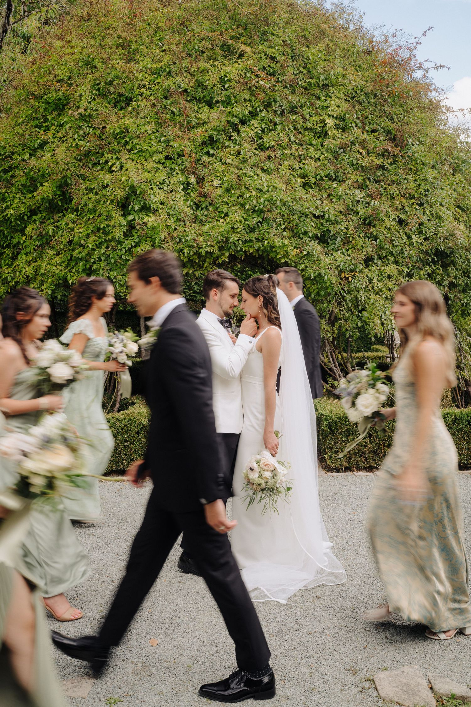 Wedding party members in motion walking and dancing on an outdoor path with greenery in background.