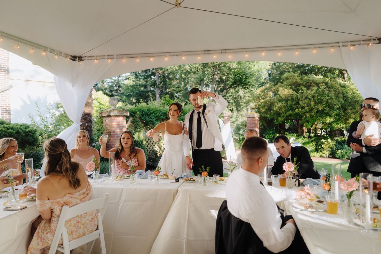 Outdoor wedding reception setup under a white tent with table settings and decor.