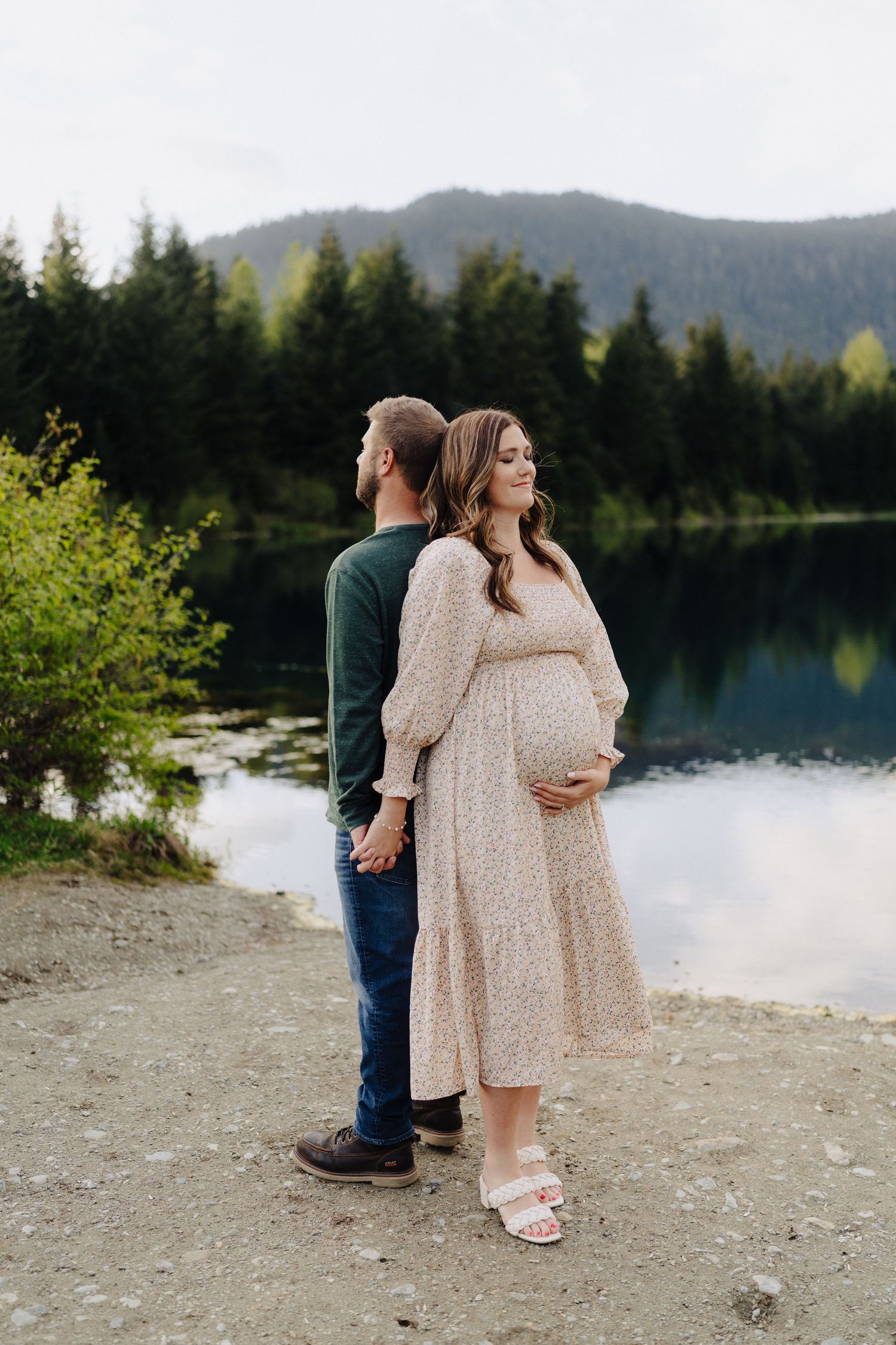 Romantic photoshoot by a pristine mountain lake with evergreen forests and cloudy skies.