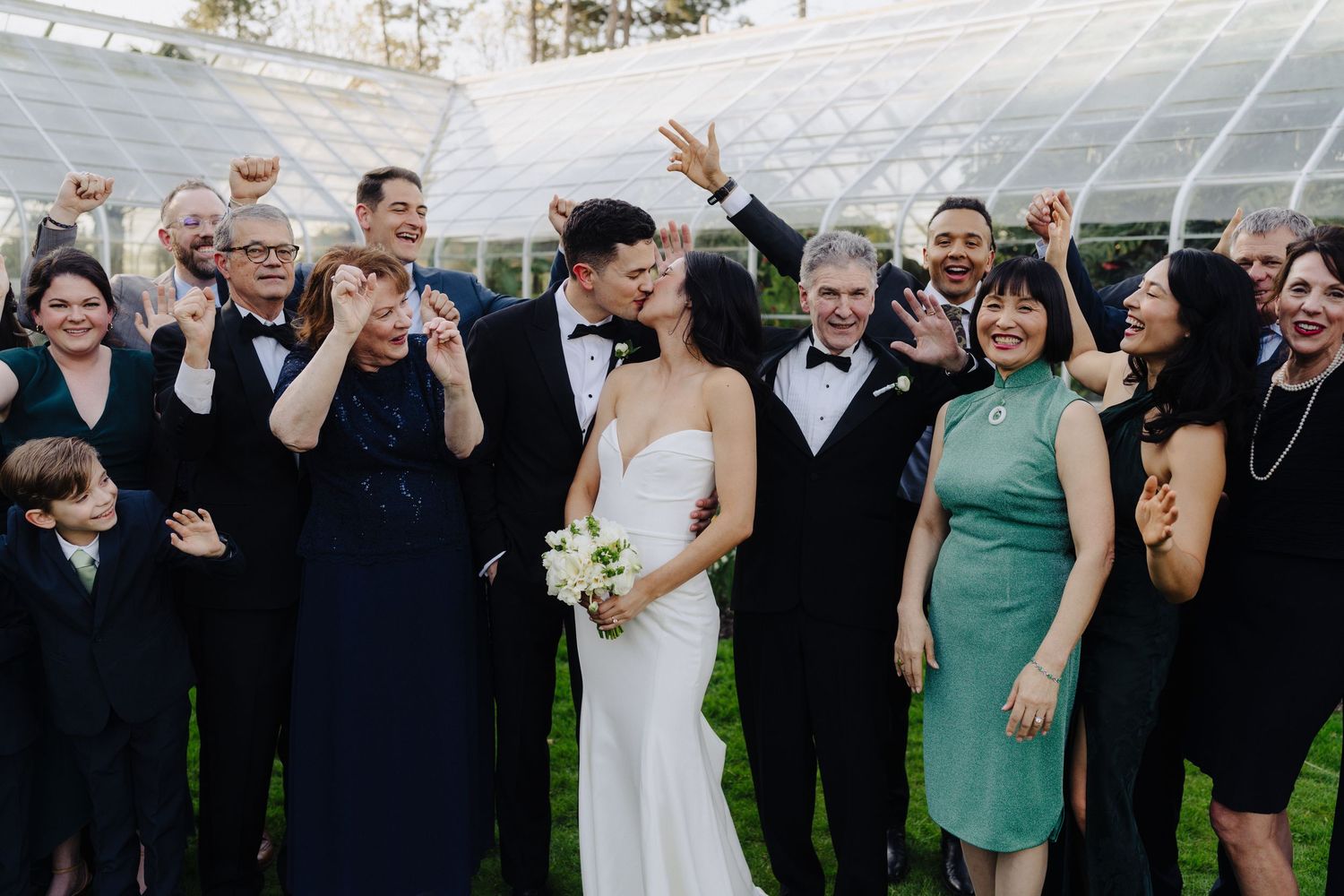 Wedding party celebrates with enthusiasm under a glass conservatory roof.