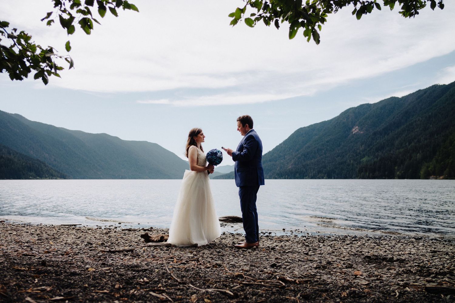 Scenic lakeside wedding photography with mountain ranges and cloudy skies in the background.