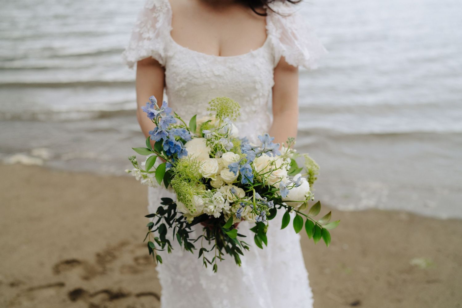 White wedding bouquet with delicate flowers and greenery against ocean background.