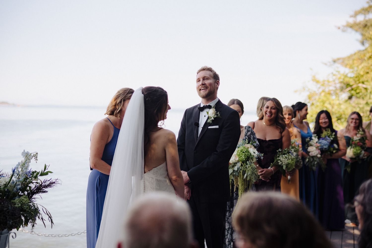 Waterfront wedding ceremony with attendants in jewel-toned dresses and natural bouquets.