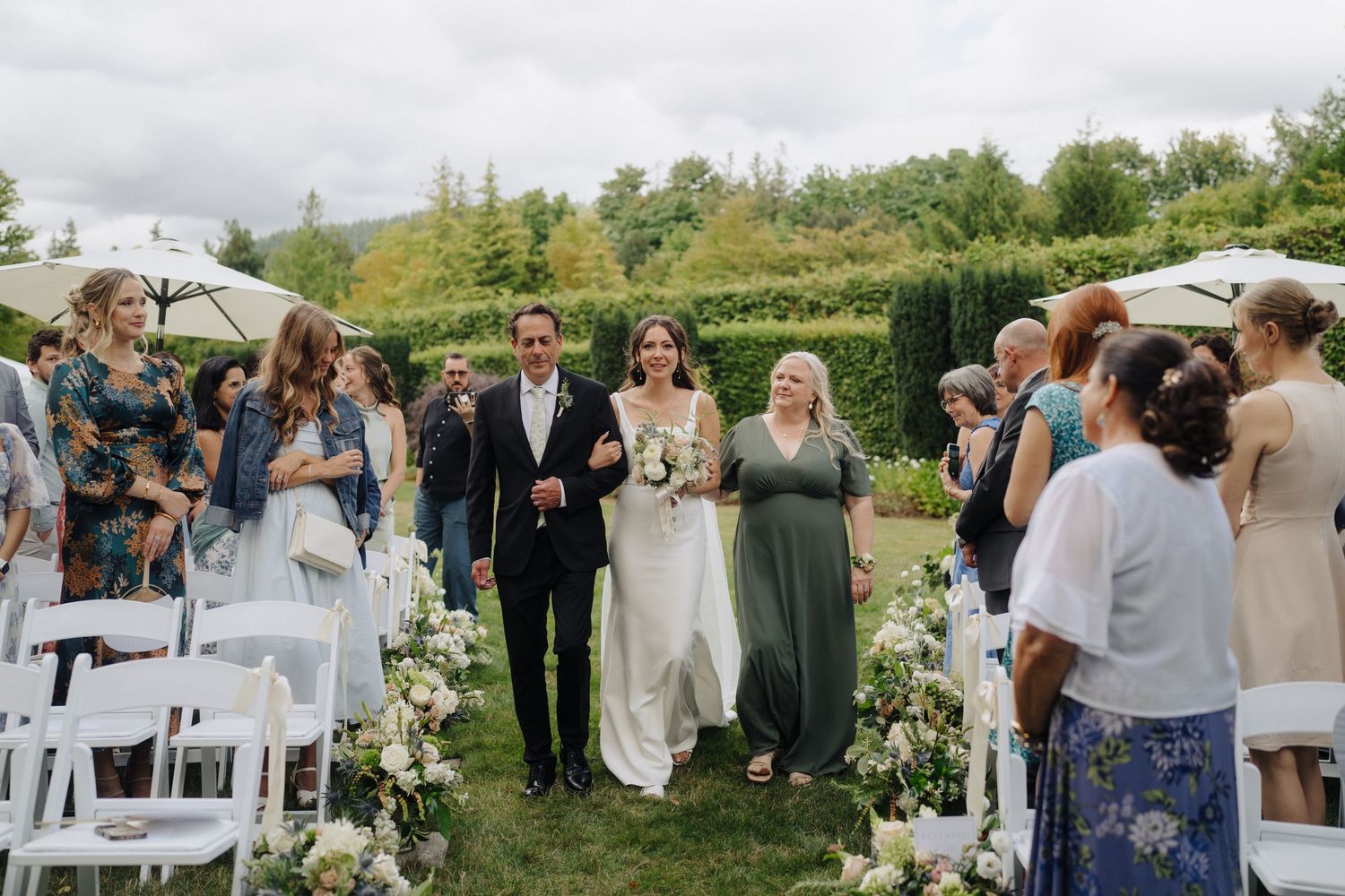 Wedding celebration outdoors with guests gathered around tables under natural lighting.