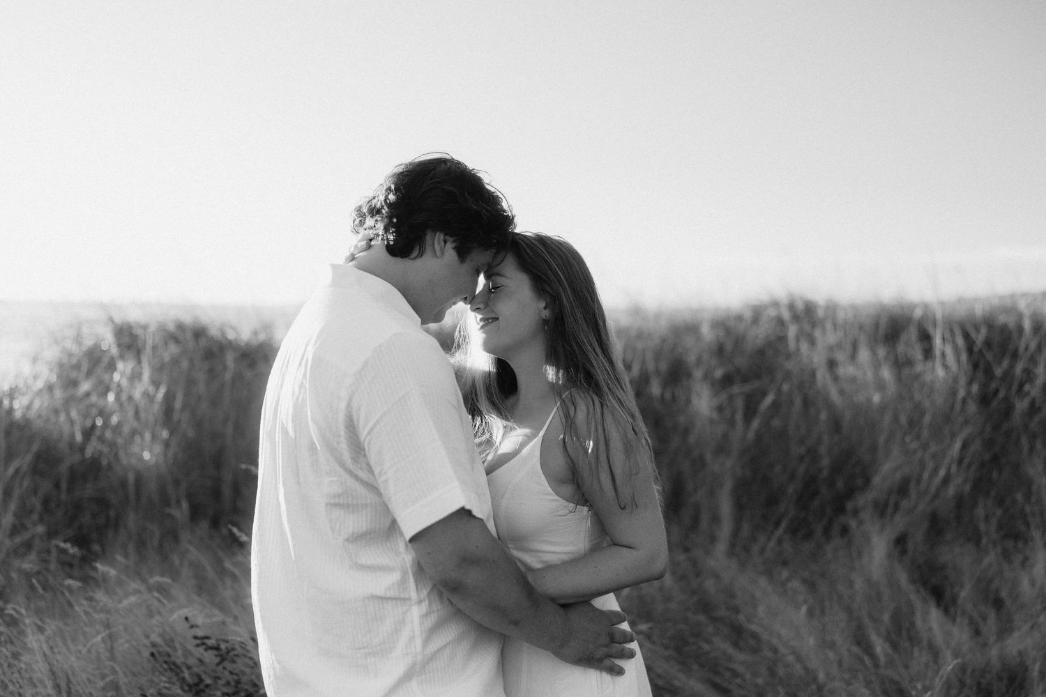 Couple embracing in a romantic moment against a scenic grassy field background in black and white.