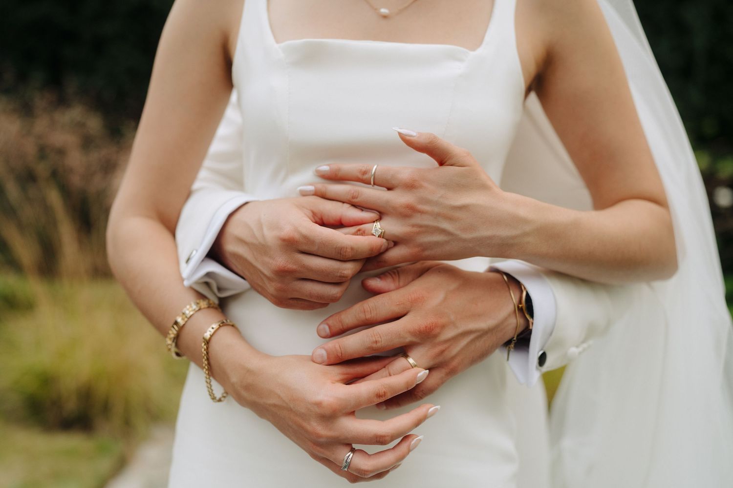 Close-up details of hands with wedding rings against a white dress.