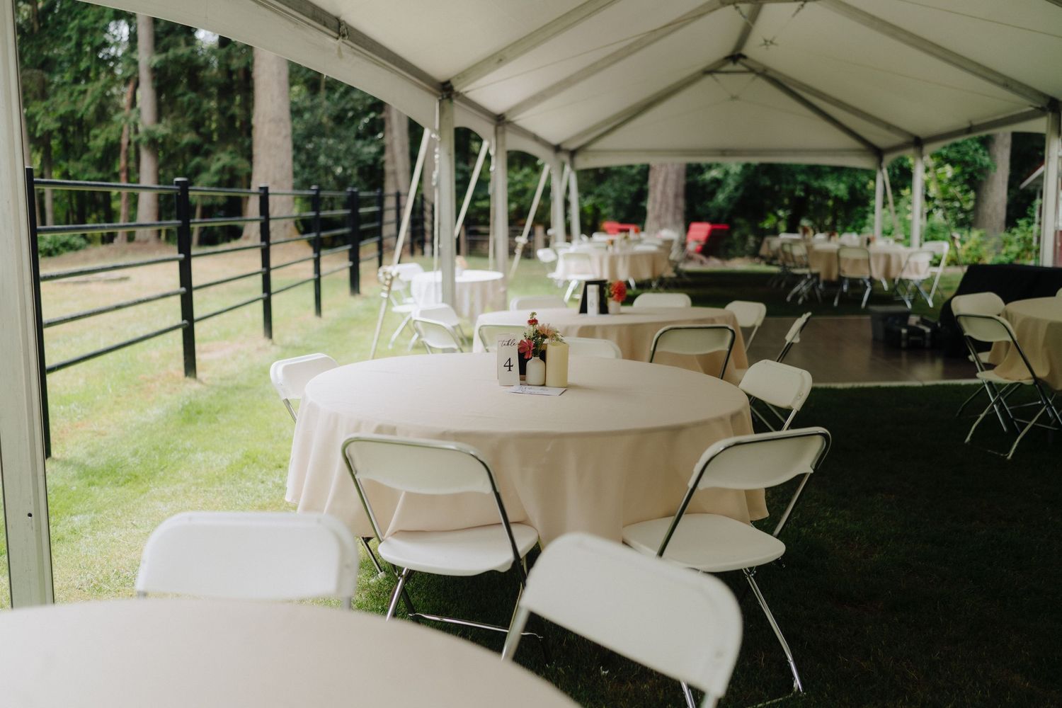 White reception tent set up outdoors with tables and chairs for wedding celebration.