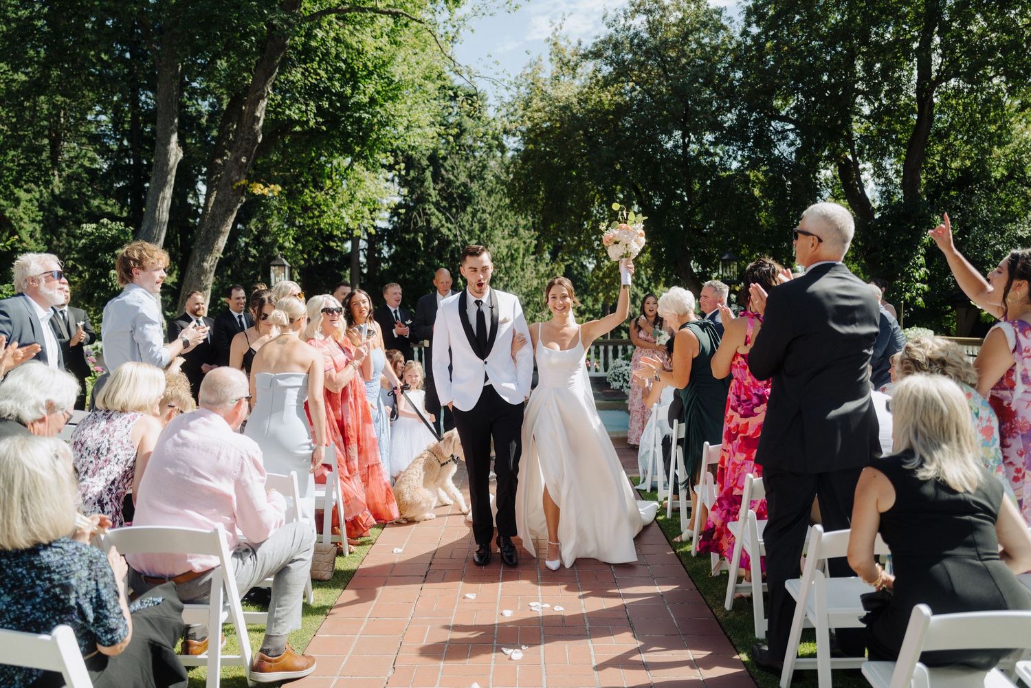 Panoramic view of an outdoor garden wedding ceremony with guests seated in white chairs.
