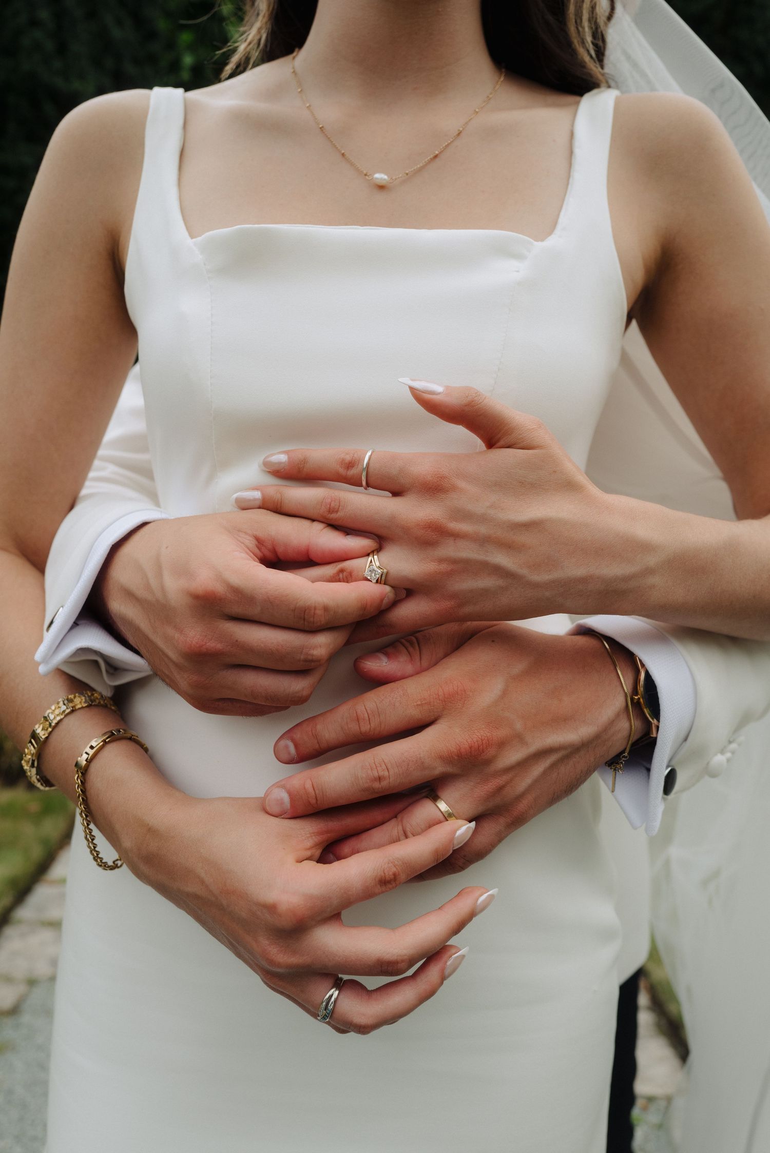 Close-up of hands wearing multiple rings and jewelry against a white dress background.