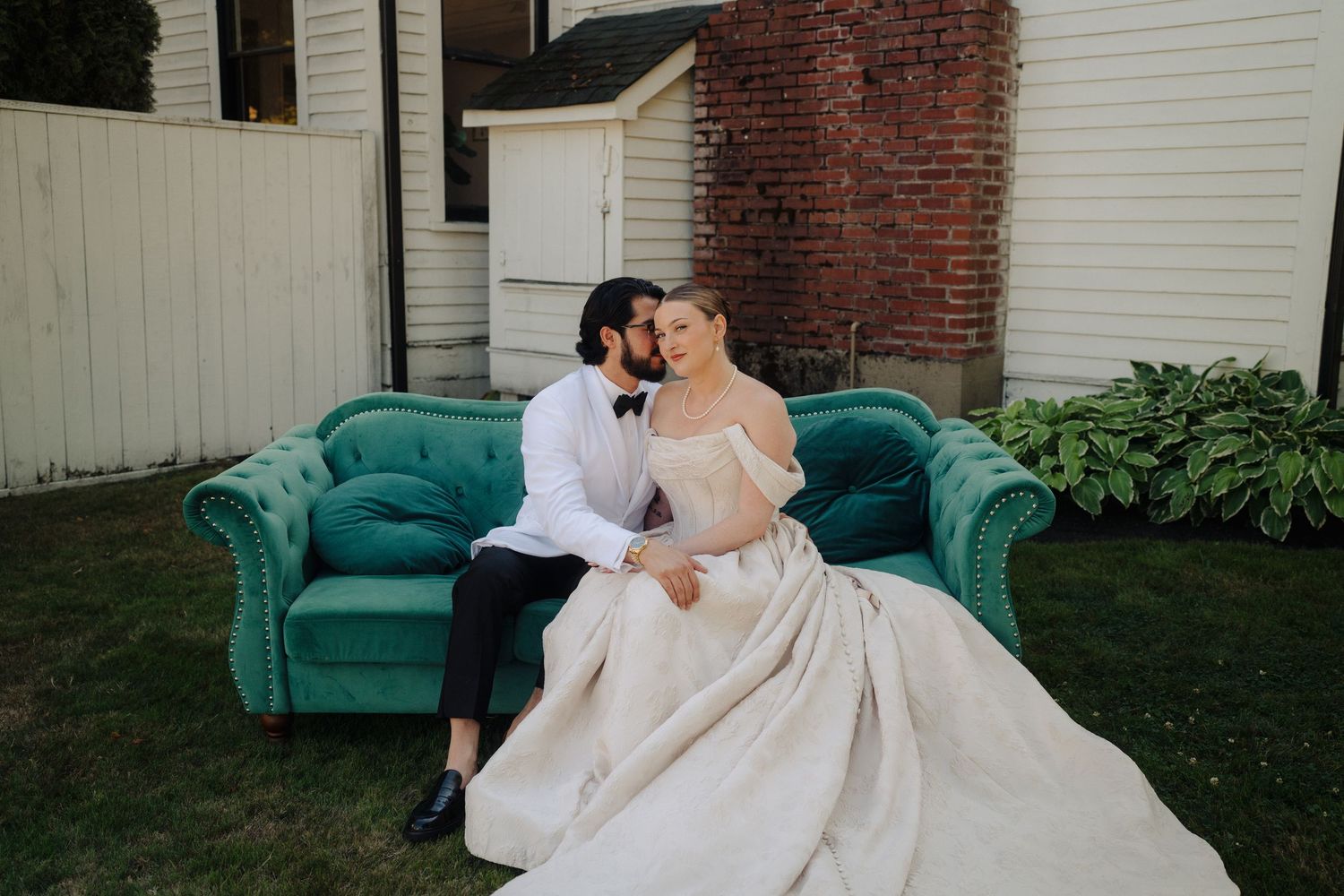 A couple shares intimate moments on a teal vintage couch outside a white house.