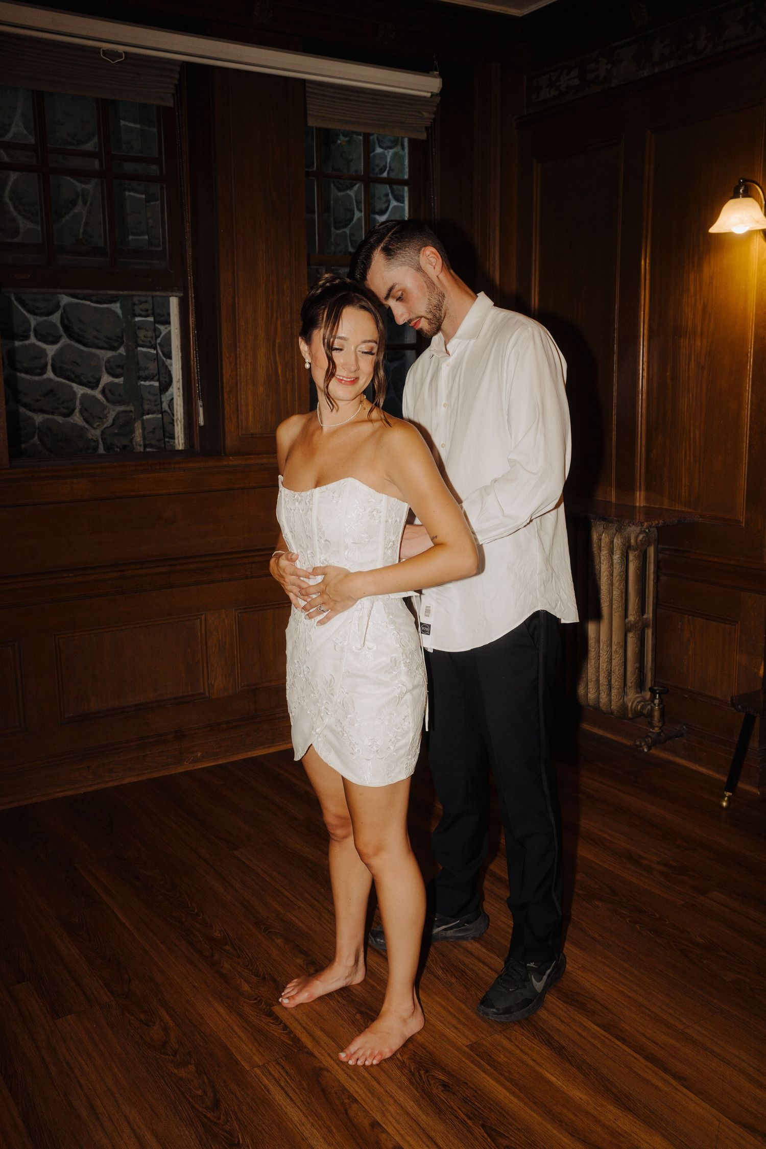 Couple dancing together on hardwood floor in dimly lit room.