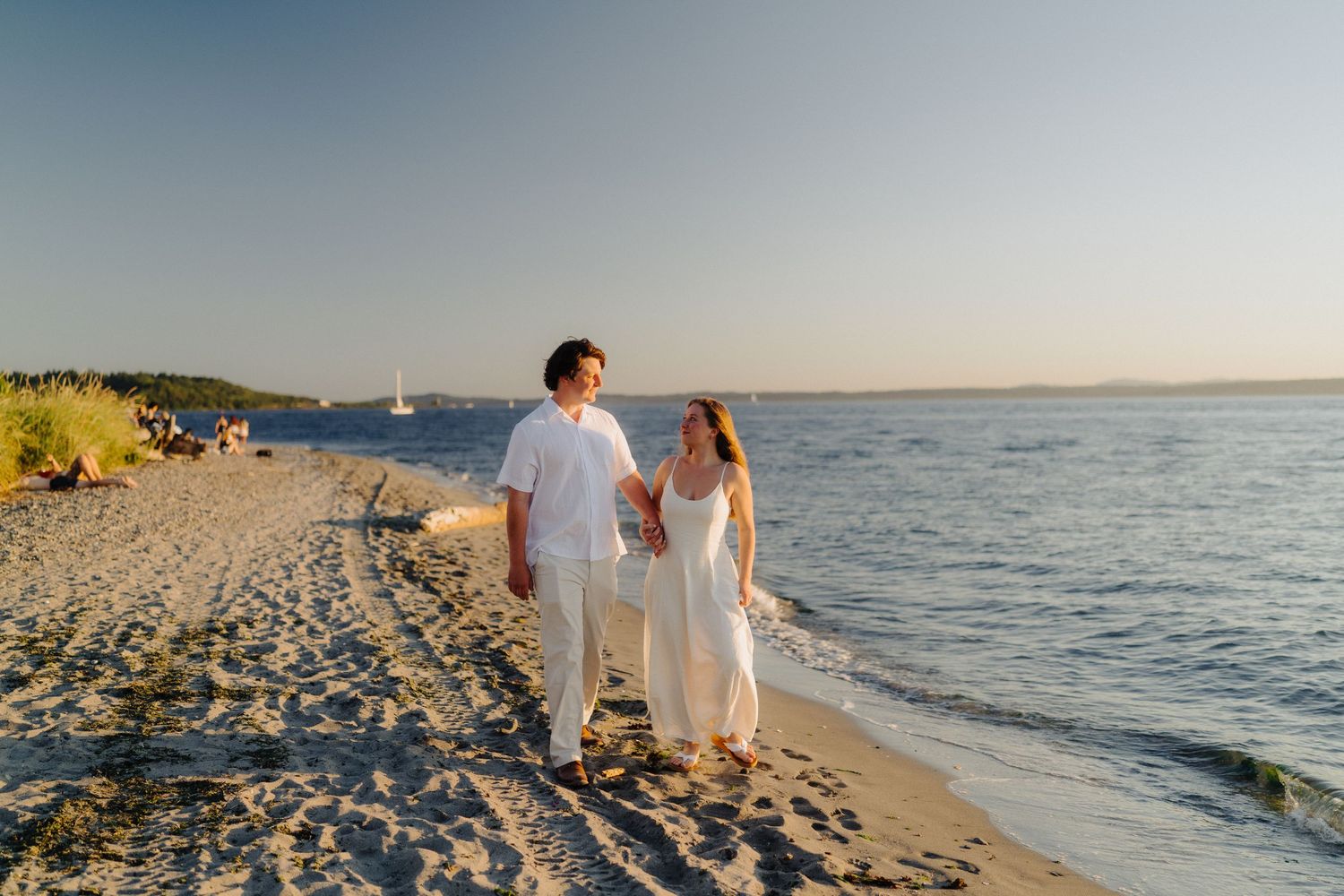 Couple walking hand in hand along a peaceful beach shoreline at dusk.