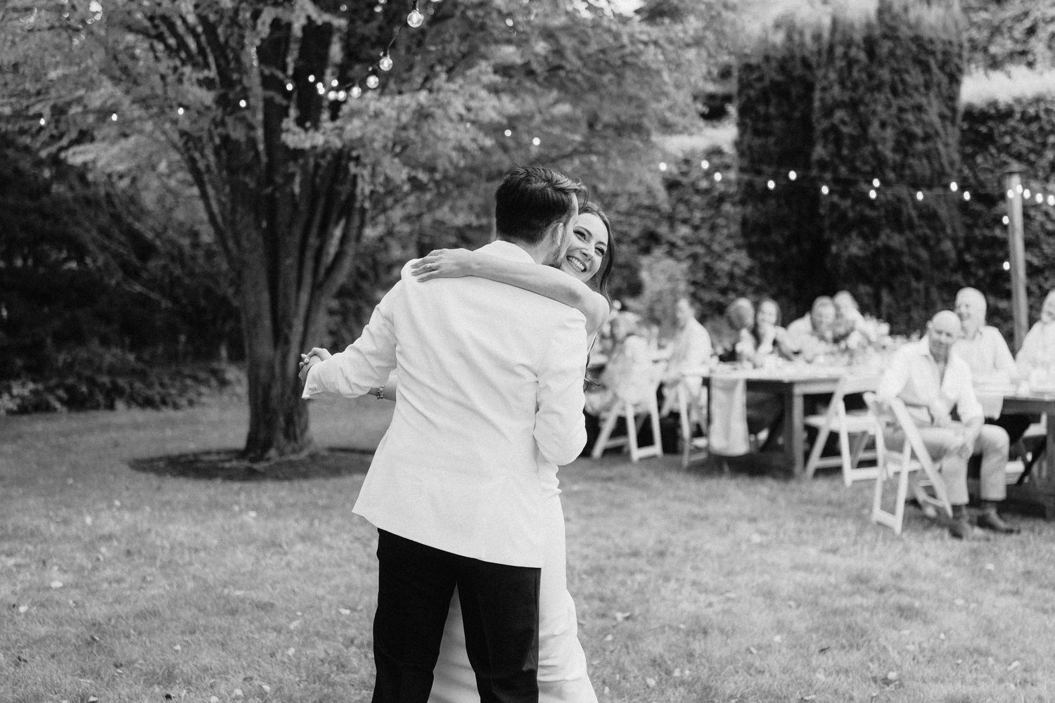 Outdoor wedding reception setup with white chairs and tables on a lawn.