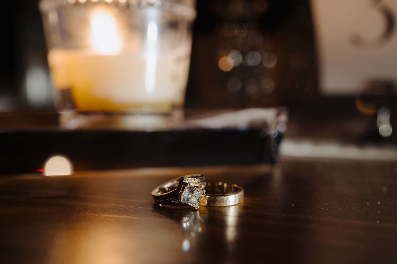Wedding rings and candles create an intimate atmosphere on a dark wooden surface.