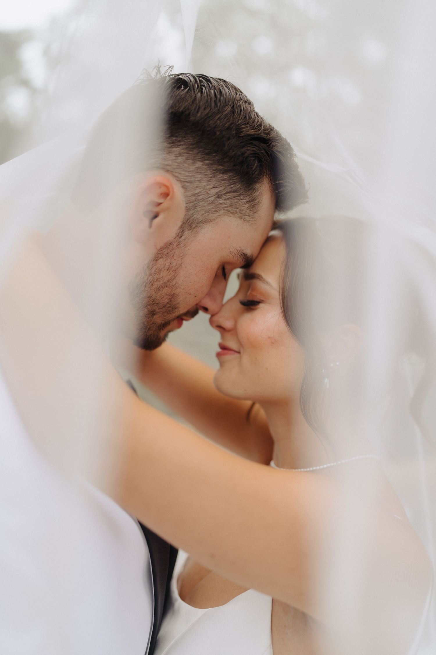 A tender moment captured through delicate white wedding veil.