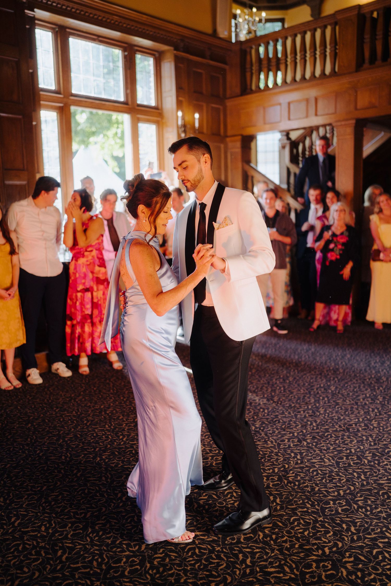 Wedding guests dancing in a grand ballroom with wooden walls and ornate details.