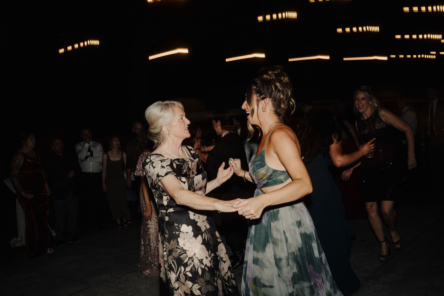 Wedding guests dancing together under dim lighting at an evening reception celebration.