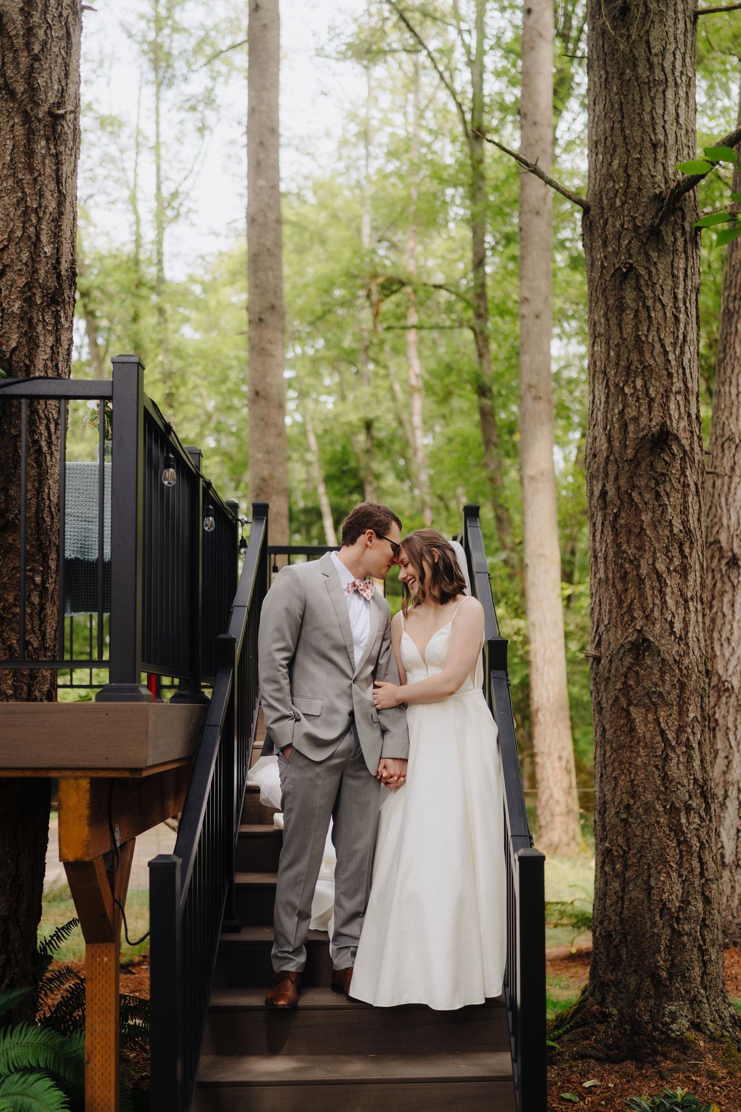 Couple shares intimate moments on a wooden deck surrounded by tall forest trees.