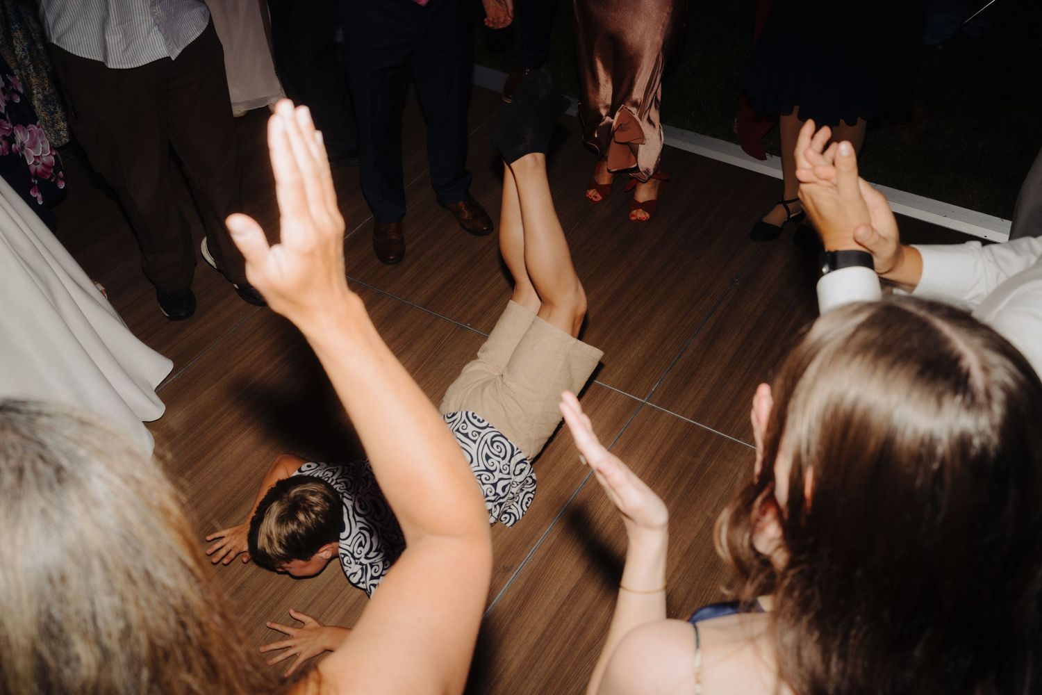 Wedding guests dancing with raised hands on wooden dance floor.