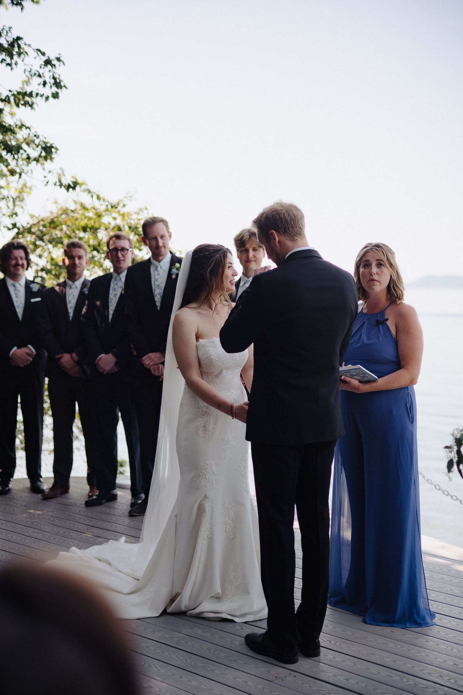Wedding ceremony taking place on a waterfront deck with attendees in formal attire.