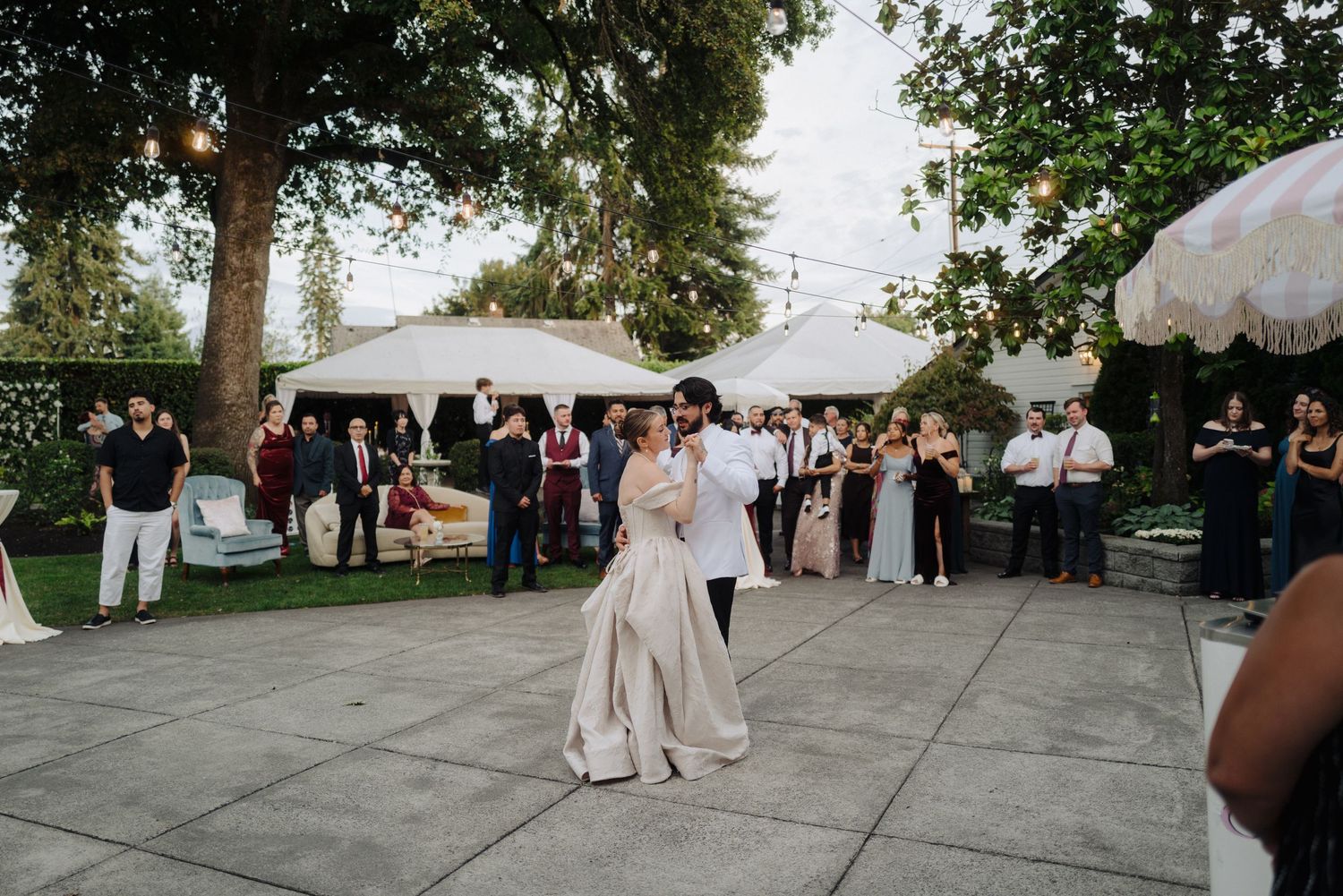 Wedding celebration on a stone patio with guests gathered under tall trees.