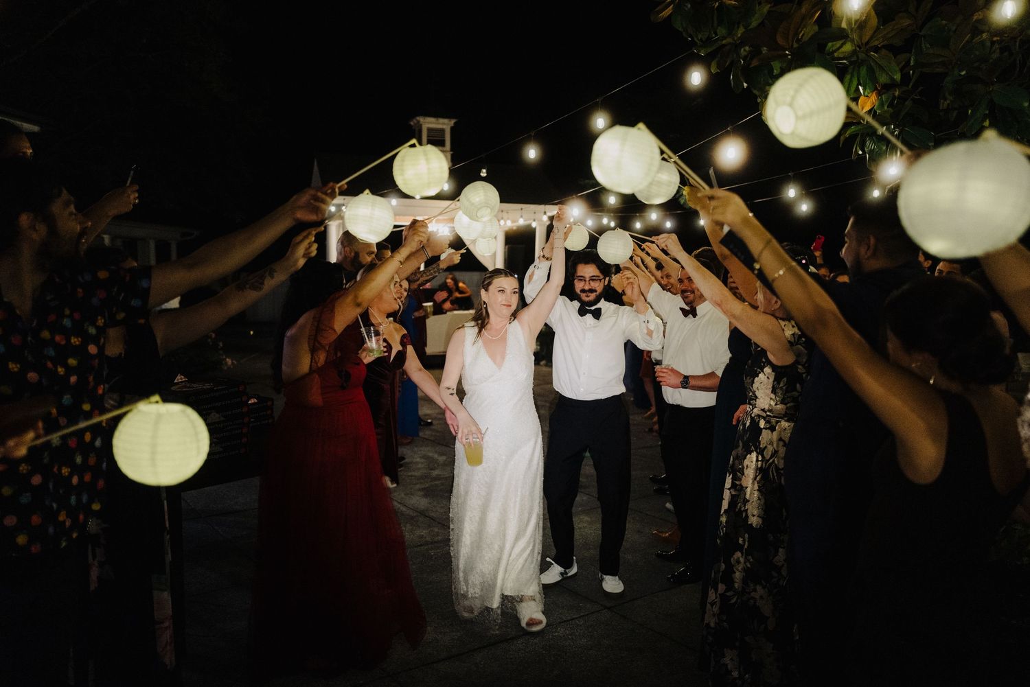 Evening wedding celebration with guests dancing under glowing paper lanterns.