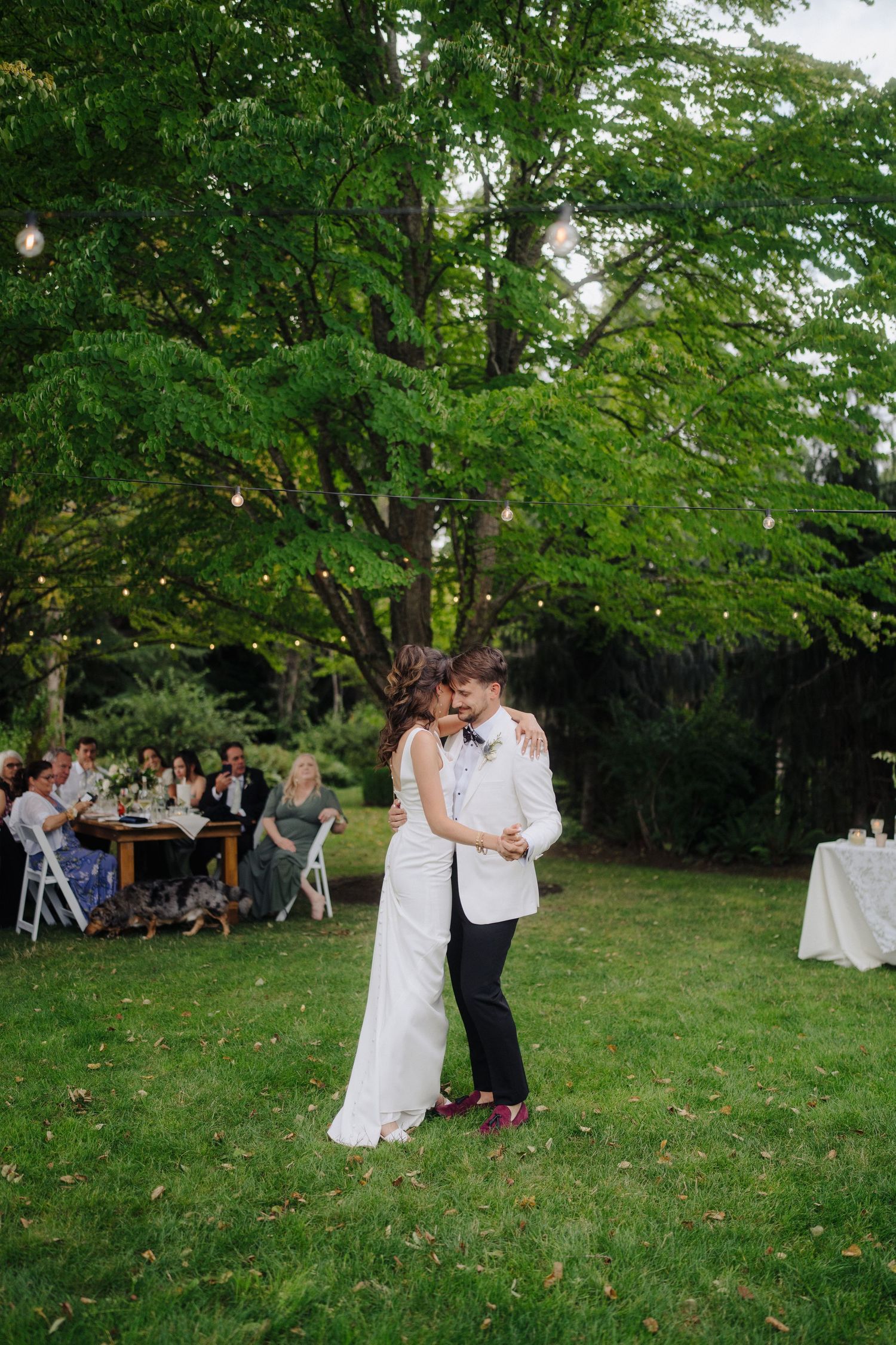Couples dance together on a lush green lawn during an outdoor wedding reception.