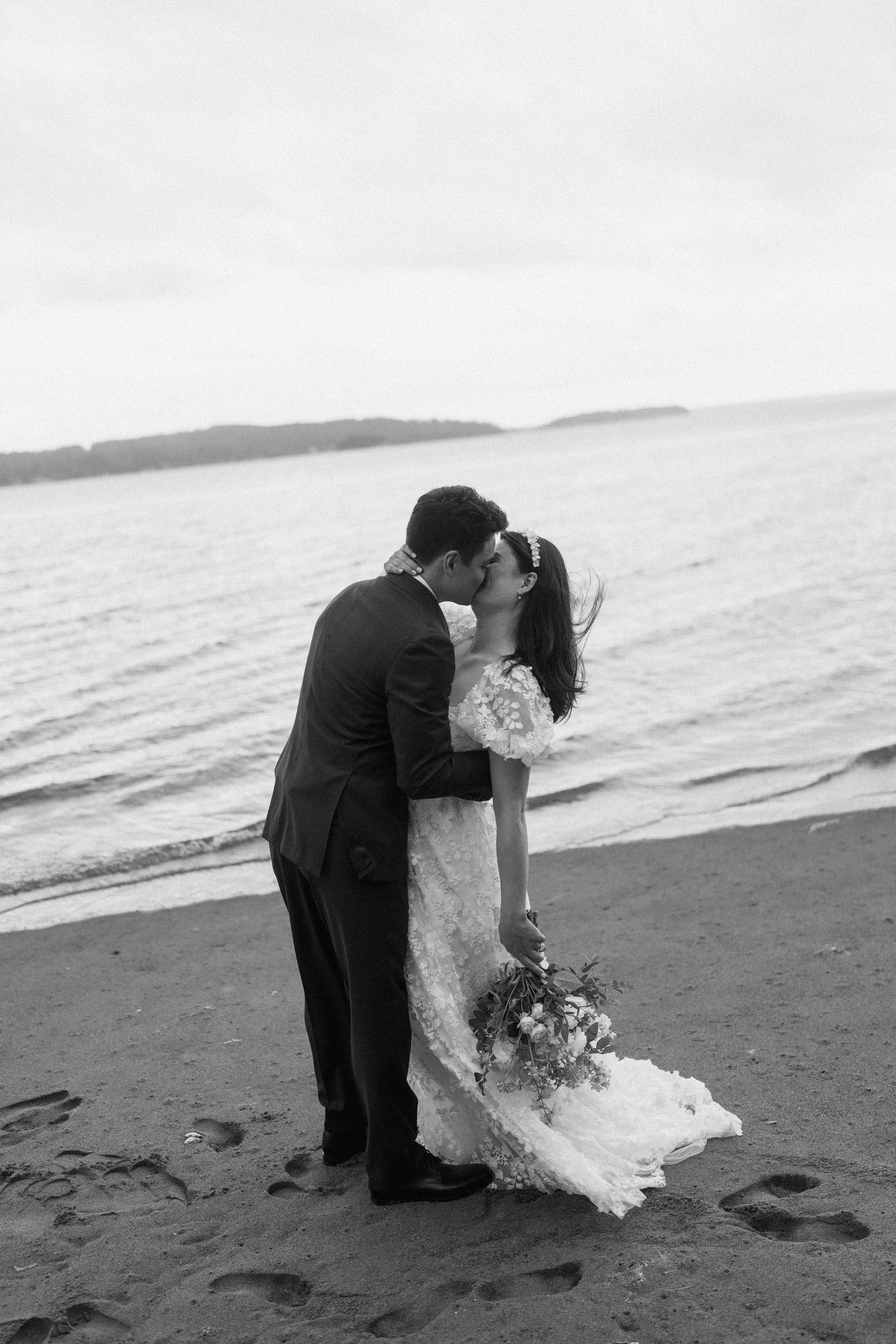 A romantic black and white wedding photo of a couple embracing on a misty beach.