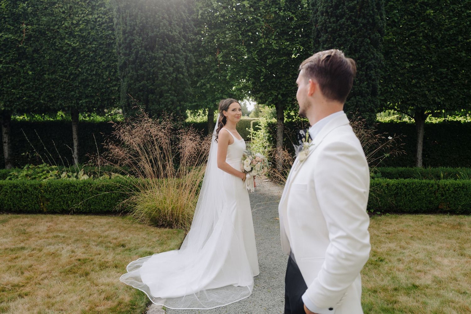 Couple shares first look moment in sunlit garden pathway.
