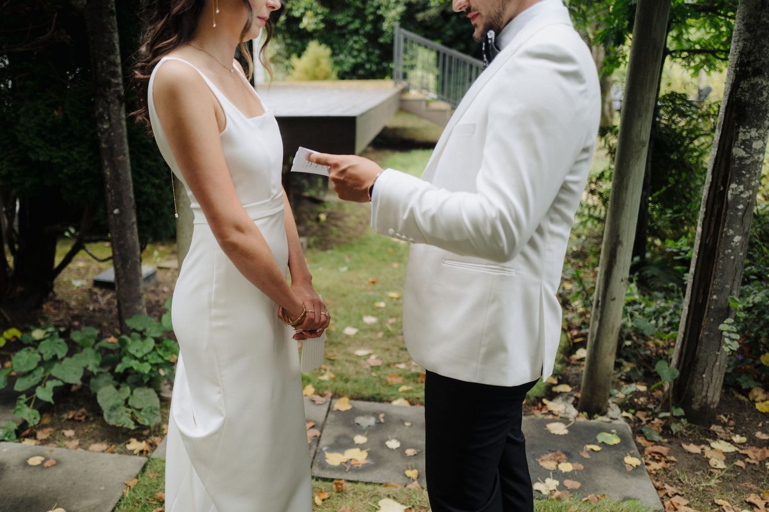 Two people in white attire share an intimate dance moment outdoors among trees and fallen autumn leaves.