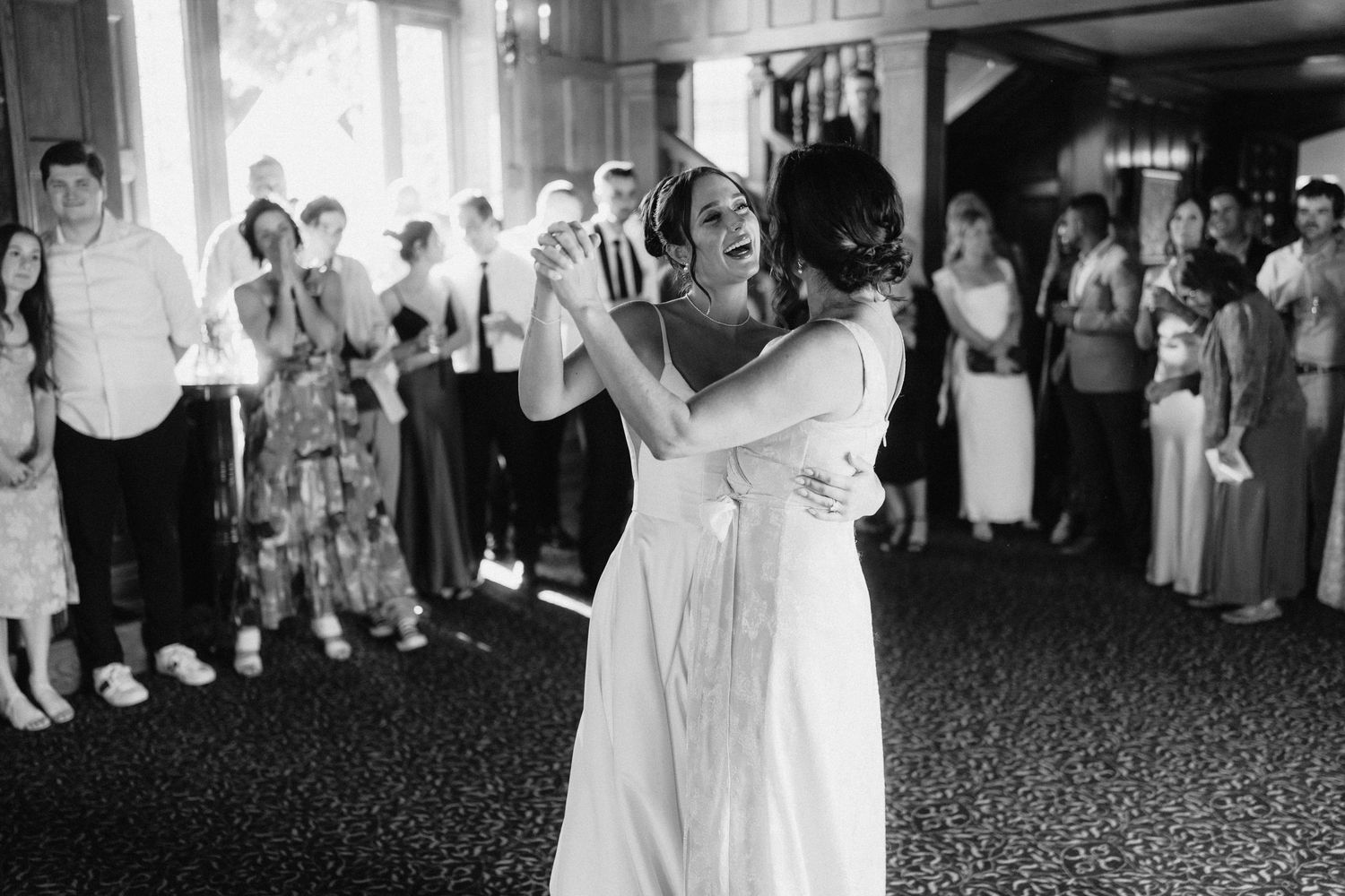 Black and white photo of wedding couple's first dance surrounded by guests.