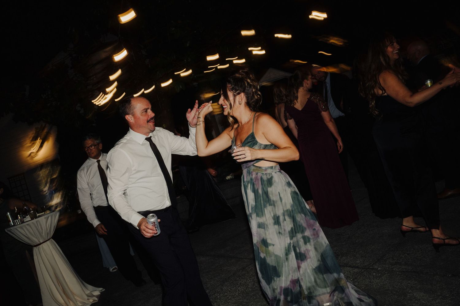 Wedding reception dance floor filled with guests dancing under dim lighting at night.
