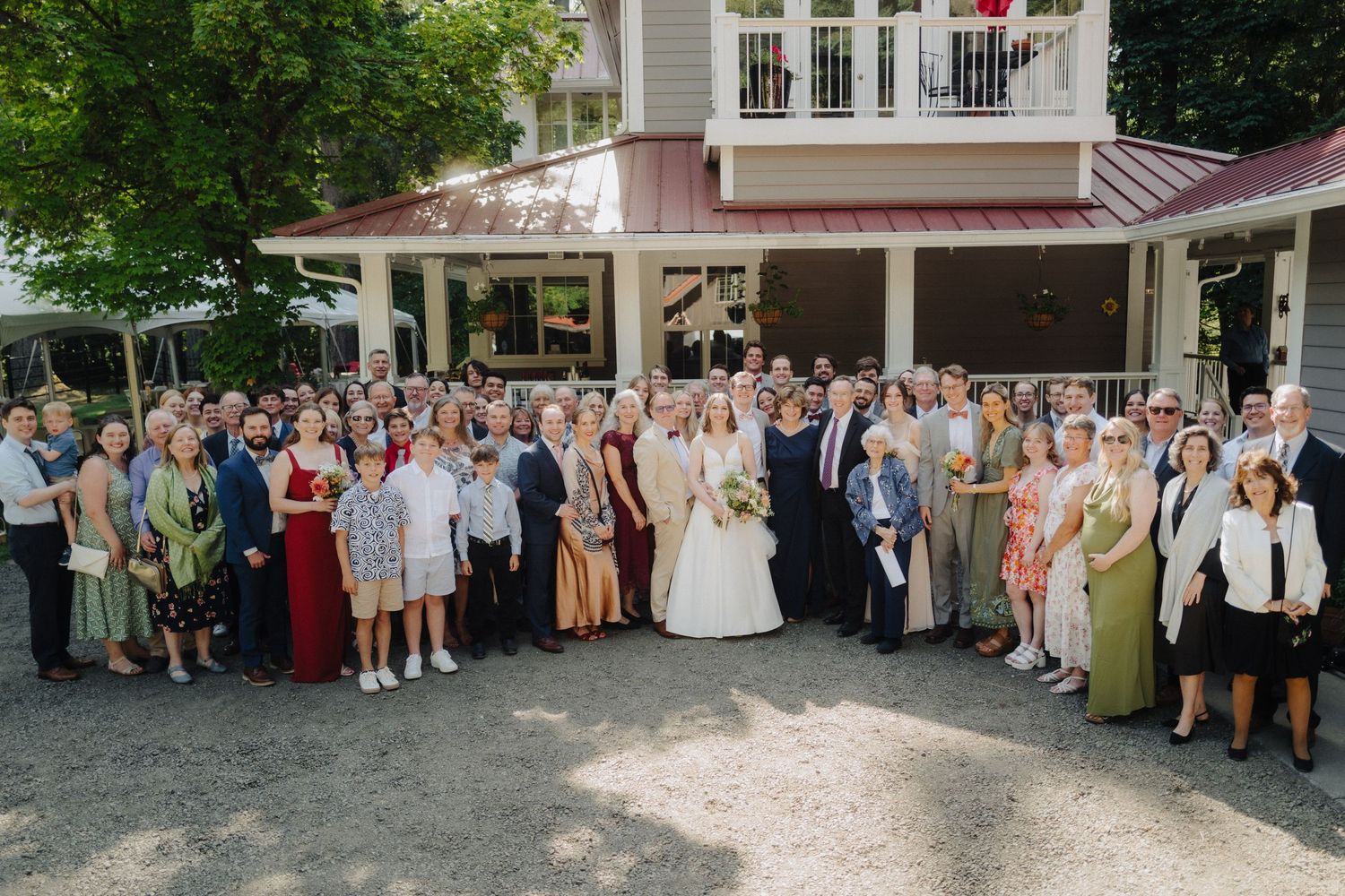 Large group wedding photo with guests gathered outside venue building.