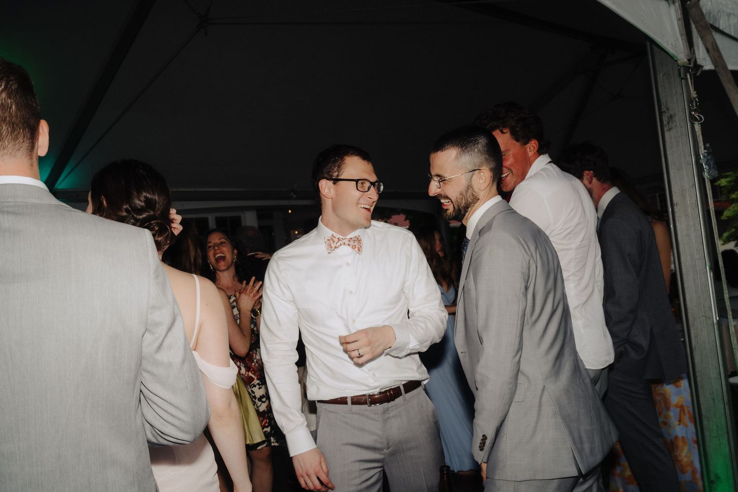 Wedding reception guests mingling under white tent with festive lighting.