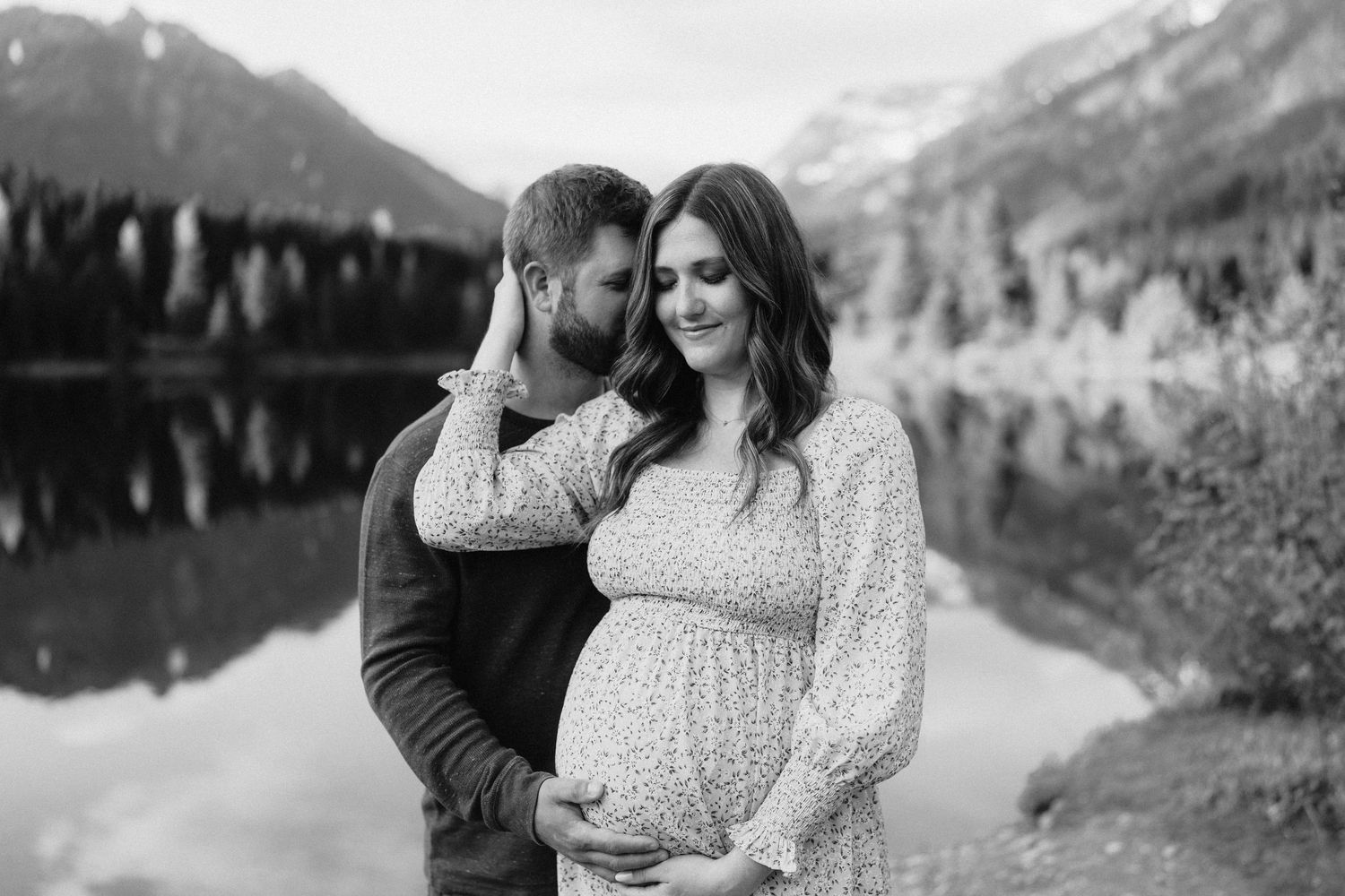 Romantic maternity portrait in black and white with mountains and lake reflecting in background.
