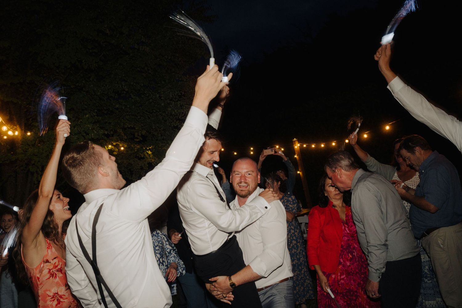 Wedding guests dance and celebrate under evening lights at an outdoor reception.