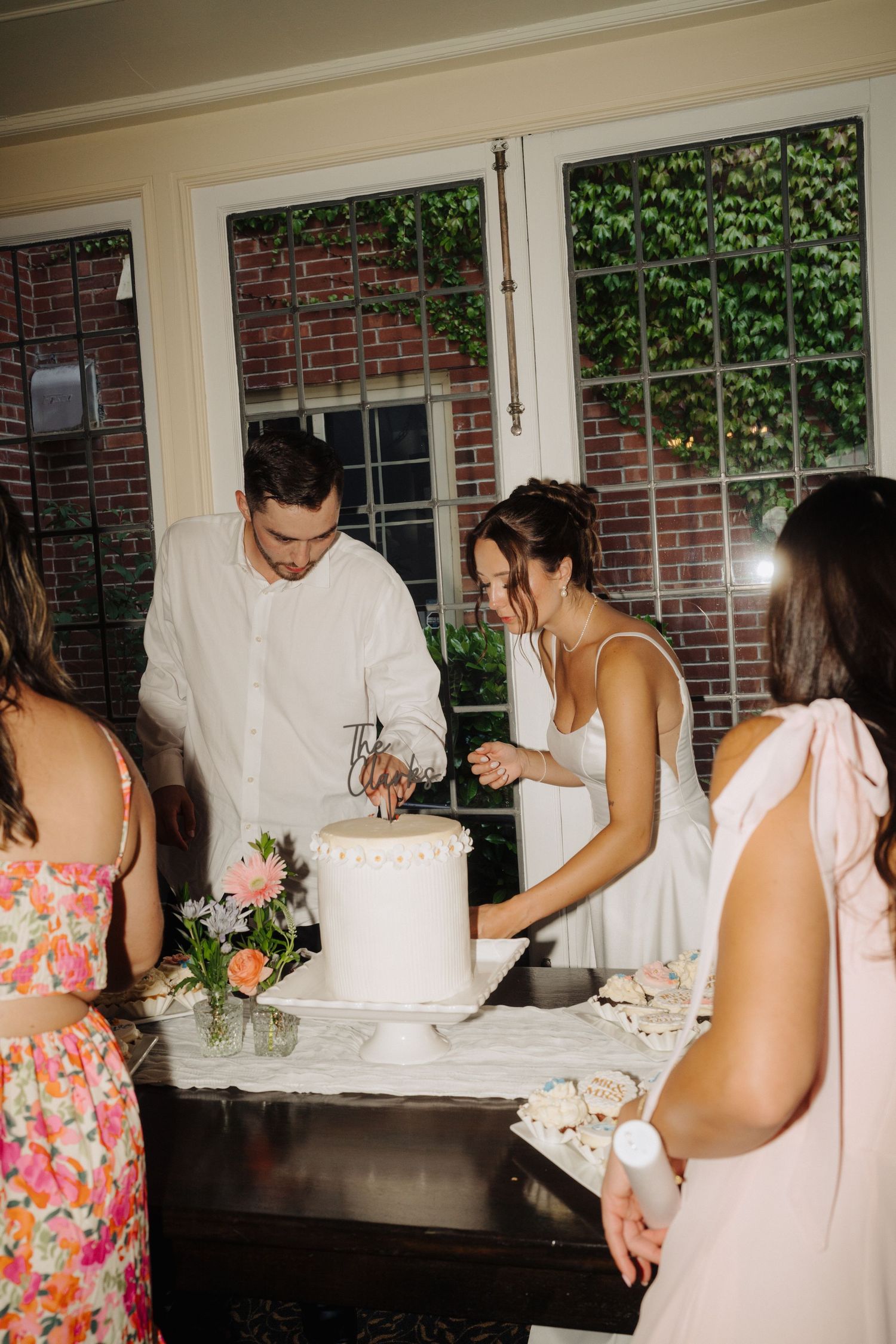 Wedding cake cutting ceremony with guests in floral dresses watching.