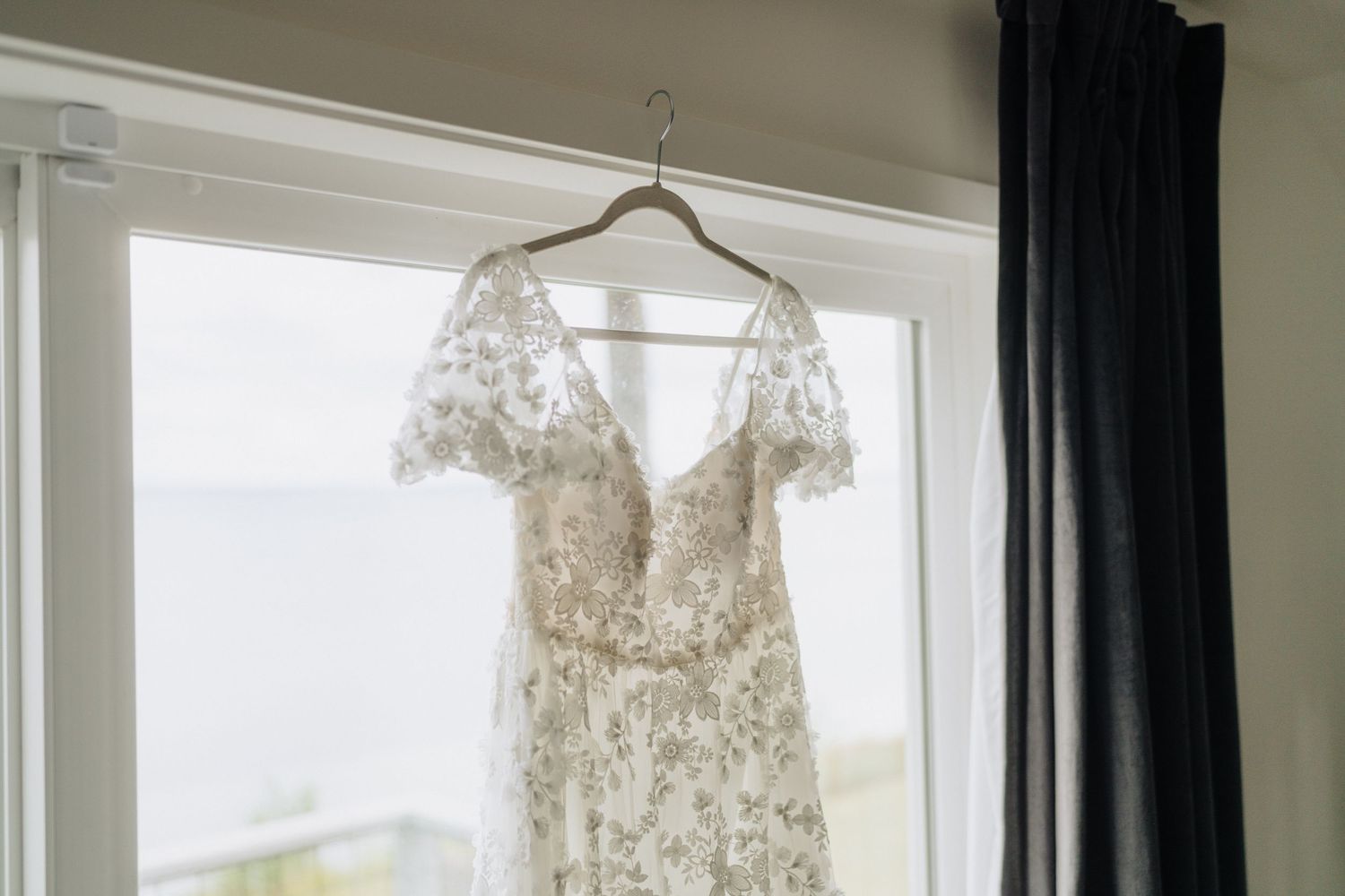 A collection of elegant white wedding dresses hanging on display in a bright room with natural lighting.