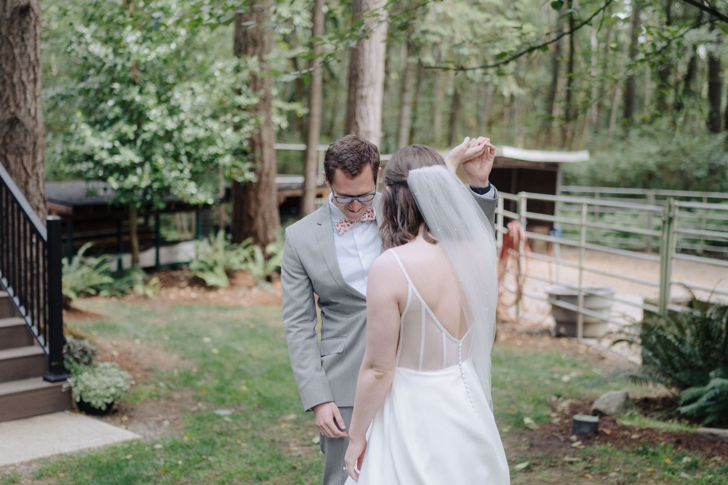 A couple shares a romantic first look moment in a wooded outdoor setting with the bride in white and groom in gray.