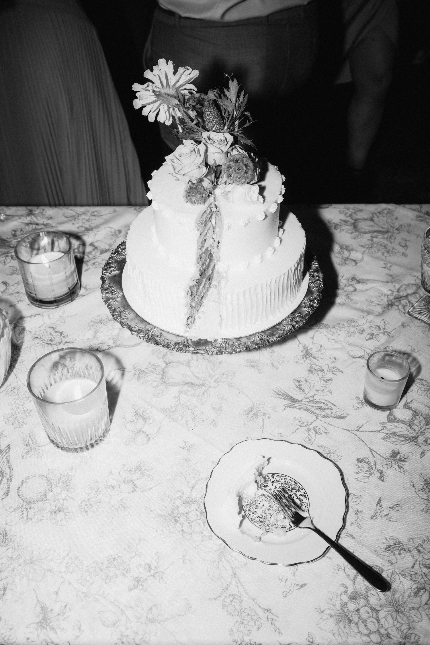 Black and white photo of wedding cake and table settings with floral details.