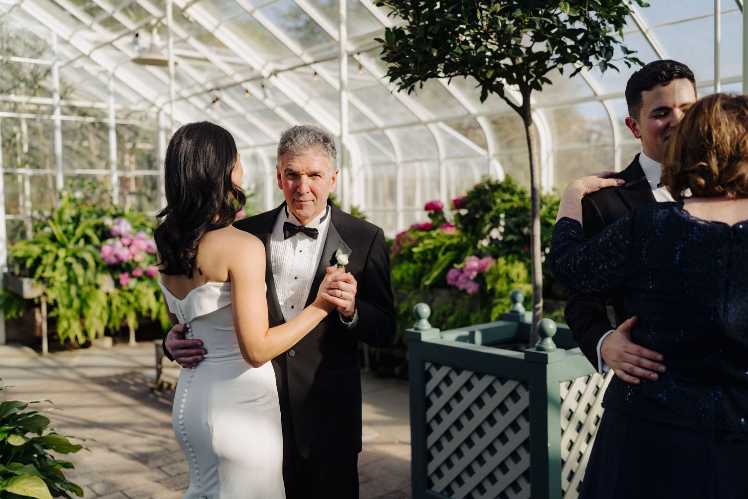 A couple shares an intimate dance together in an elegant greenhouse setting surrounded by lush greenery and natural light.