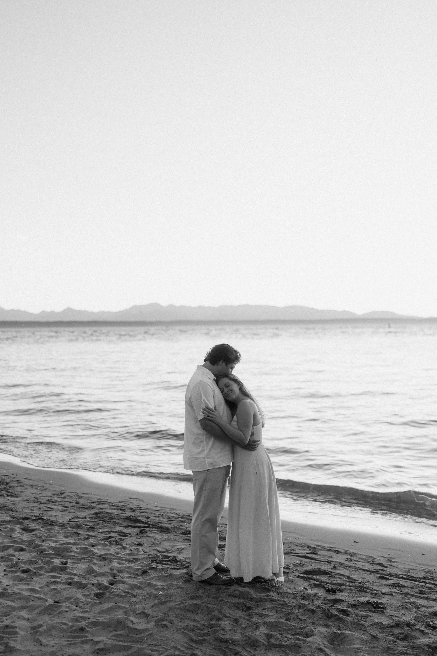 A black and white photograph of a couple in an intimate embrace by the ocean.