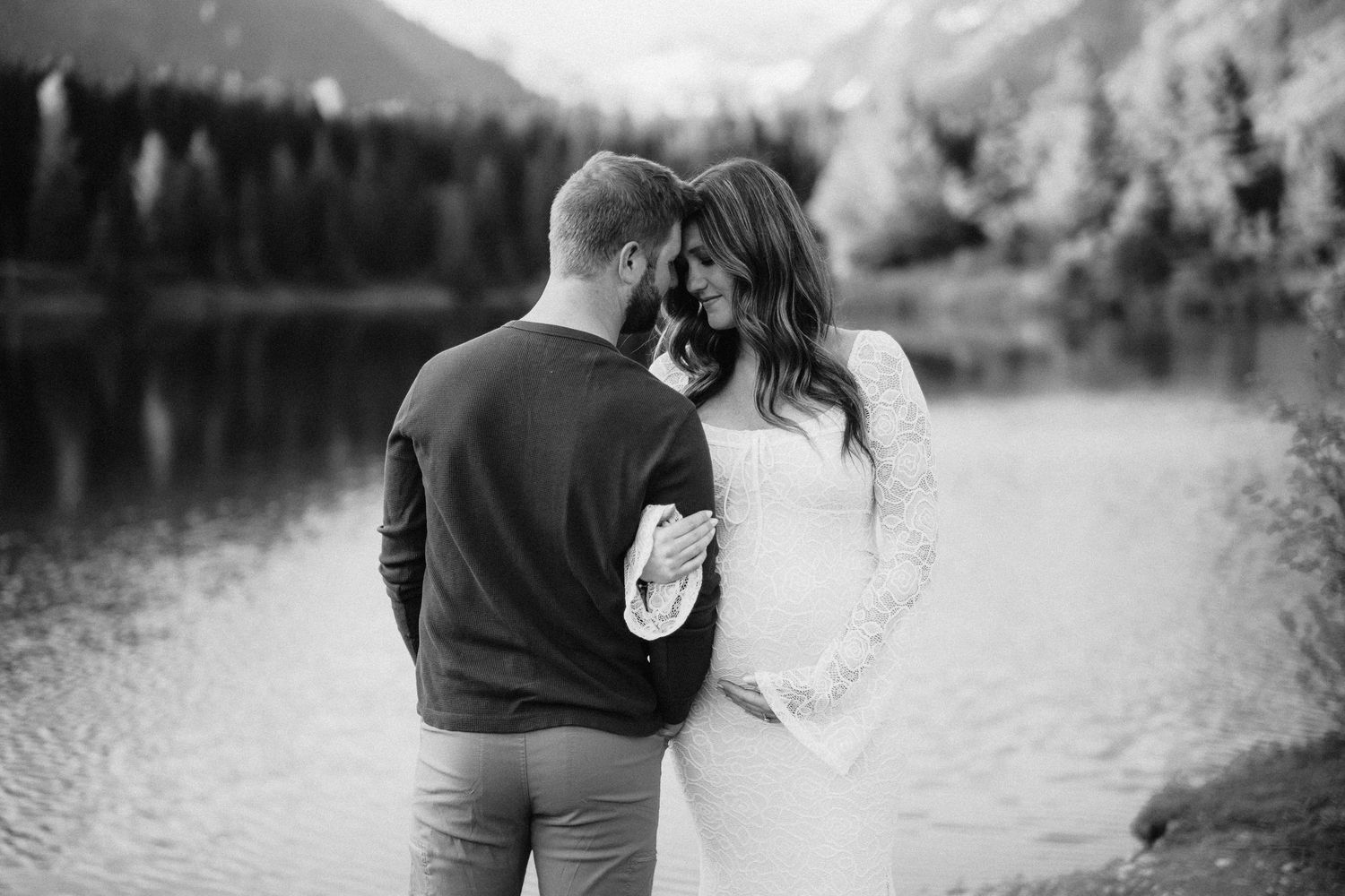A black and white photo of a couple sharing an intimate moment by a mountain lake.