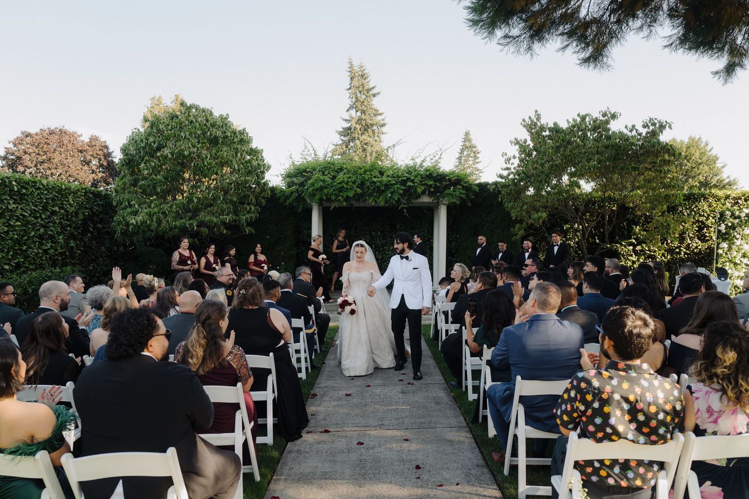Outdoor wedding ceremony setup with white chairs and natural greenery backdrop.