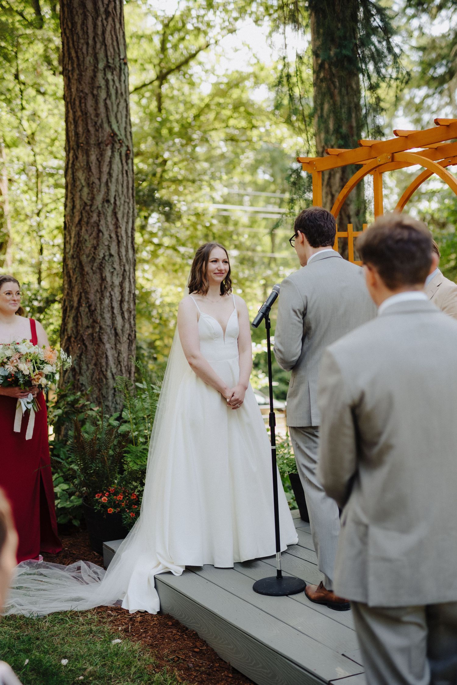 Outdoor wedding ceremony under tall pine trees with wooden arch and floral decorations.